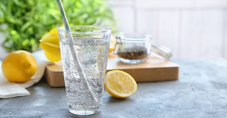 Glass jar of chia seed water recipe with lemon slices and fresh ginger on a light wooden surface